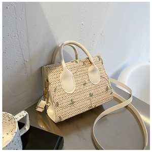Detailed view of floral embroidery on a straw crossbody bag with white leather handle
