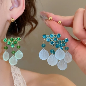 Close-up of dangling zircon and glass shell tassel earrings with blue resin pendants