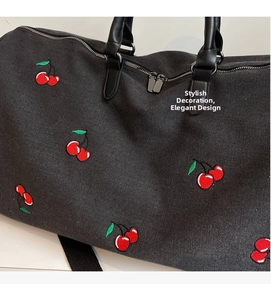 Close-up of black canvas tote bag featuring red cherry embroidery and silver zippers