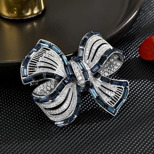 Macro shot of silver bow brooch with dark blue emerald-cut stones and crystal pavé