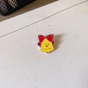 Close-up of a cartoon yellow bell brooch with a red bow on a white textured background