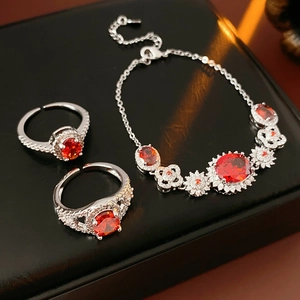 Detail of silver clover bracelet and flower rings with sparkling red zircons on black leather