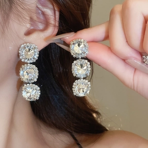 Detail of elegant silver square crystal earrings worn by a model in soft lighting