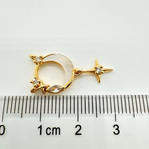 Vue macro d'un pendentif lune en or 18K avec nacre et zircons à côté d'une règle graduée