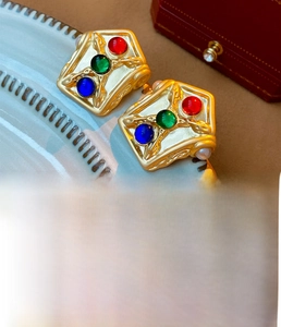 Close-up of vintage gold plated earrings with colorful resin stones on a ceramic plate