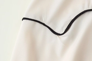 Gros plan détaillé des coutures contrastées et du passepoil noir sur la robe chemise sans manches