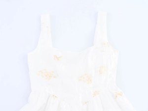 Dettaglio del tessuto bianco con ricami floreali dorati e texture elegante del vestito
