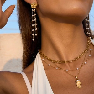 Gros plan de boucles d'oreilles en perles et collier Hamsa portés par un mannequin