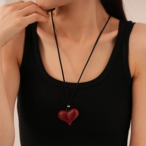 Close-up of red resin heart pendant with black cord on a ribbed sweater