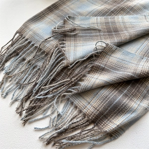 Close-up of soft plaid scarf texture with blue and beige patterns and fringe details