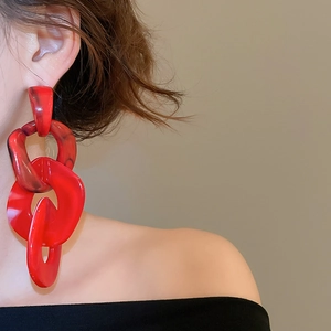 Detailed view of red acrylic chain drop earrings with black marble pattern on model