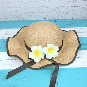 Detail of wide brim straw sun hat featuring decorative white plumeria flowers and brown ribbon