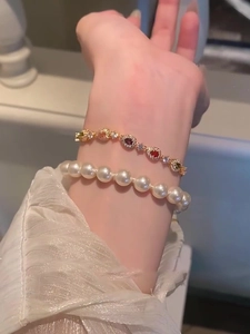 Detail of layered white pearl bracelet and gold chain with colorful zircon gemstones