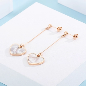 Macro detail of rose gold heart drop earrings with white iridescent shell inlay on stand