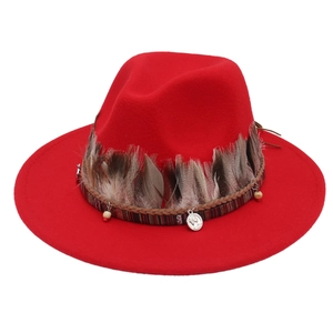 Detail eines roten Fedora-Hutes mit Federn, gewebtem Ethno-Band und einem Metallanhänger