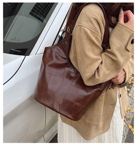 Detail van vintage bruine leren tote bag met vierkante textuur gedragen op de schouder