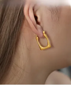 Detailed close-up of a gold U-shaped earring with textured surface on female model
