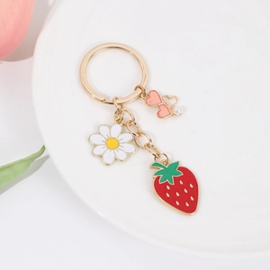 Close-up of strawberry, daisy and heart charms on a gold keychain on a white plate