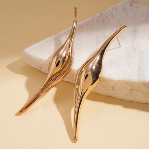 Close-up of golden streamlined curved leaf earrings on marble, showing mirror finish