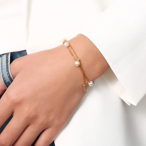 Gros plan d'un bracelet double couche en acier doré avec perles porté au poignet