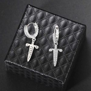 Macro shot of silver dagger cross earrings with zircon pavé on black leather surface
