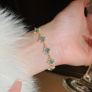 Close-up of a gold-plated link bracelet with square blue zircons worn on a wrist