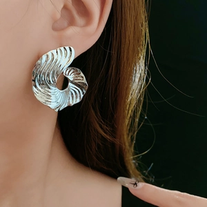 Detail of silver spiral shell-shaped earrings on a model showing modern textured design
