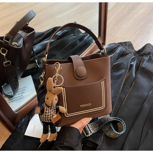 Detailed view of brown bucket bag with rabbit charm and geometric patterned strap