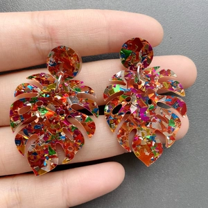 Detailed view of monstera leaf earrings with colorful glitter sequins and gold foil
