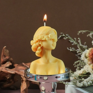 Detailed yellow blindfolded goddess candle on silver base with vintage floral decor
