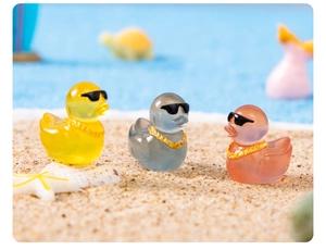 Close-up of three colorful resin mini ducks with sunglasses in a beach scene