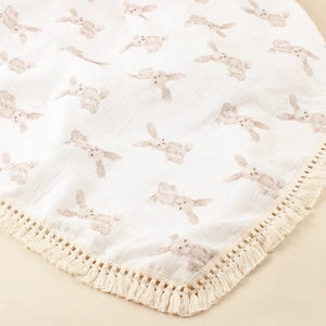Close-up of cotton baby swaddle blanket featuring watercolor rabbit print and fringe trim