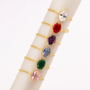Set of gold chain rings with colorful oval zircons displayed on a cylinder stand