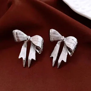 Textured silver bow earrings with vertical brushed finish on luxury dark red velvet