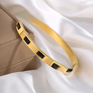 Detail of gold-plated open bangle featuring rectangular black stone inlays on silk background