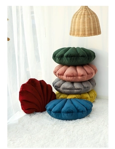 Multiple colorful velvet shell-shaped cushions stacked in a bright, cozy living room scene