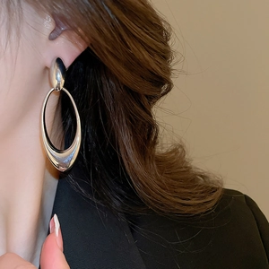 Polished silver double oval hollow drop earrings worn by a model in casual attire