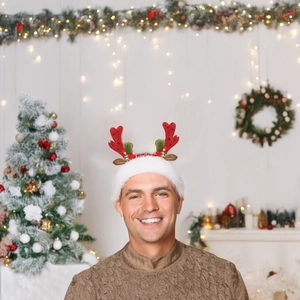 Man wearing plush Christmas reindeer headband with red sequins and bells in a festive room