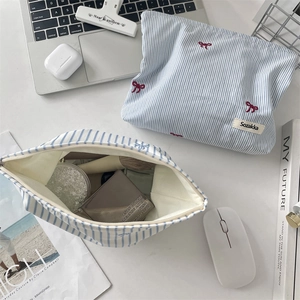 Trousse à maquillage rayée bleu et blanc avec broderie nœud rouge sur un bureau épuré