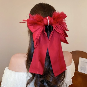 Detail of red satin bow hair claw clip with feathers and pearls on dark wavy hair