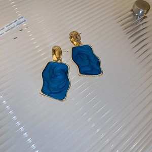Dettaglio ravvicinato di orecchini a onde in resina blu reale con bordi dorati lucidi