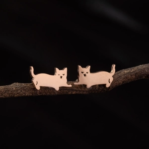 Detailed macro view of rose gold cat stud earrings resting on a rustic wooden branch