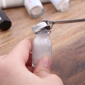 Hand using a metal tool to open small glass vials containing white powder for medical use