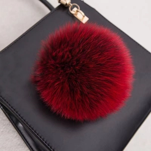 Vue macro d'un pompon en fourrure rouge duveteux avec fermoir doré sur un sac noir