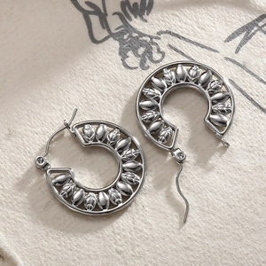 Macro shot of silver C-shaped hoop earrings featuring intricate leaf relief on art paper