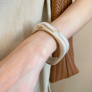 Nahaufnahme eines dicken, beige-braun marmorierten Harz-Armreifs am Handgelenk getragen