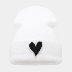 Detailed close-up of white ribbed knit beanie with a black heart embroidery patch