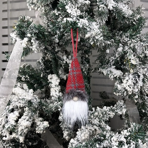 Christmas gnome ornament with red plaid hat hanging on a snowy tree branch