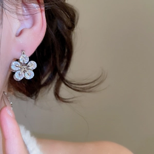 Macro view of silver floral earrings with zircon petals worn by a model
