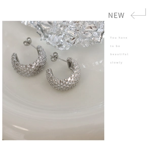 Close-up of silver C-shape earrings with inlaid zircon on white porcelain plate